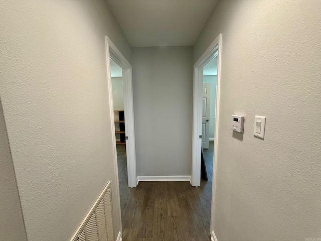 hallway featuring visible vents, baseboards, dark wood-style floors, and a textured wall