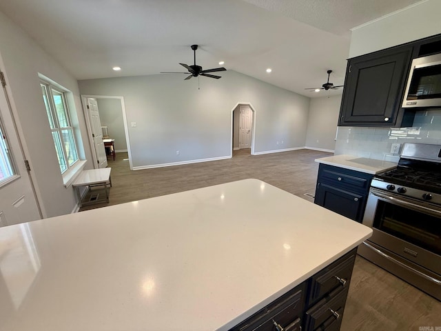 kitchen featuring appliances with stainless steel finishes, light countertops, decorative backsplash, lofted ceiling, and dark cabinets