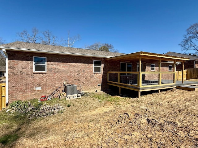 rear view of house with cooling unit, brick siding, roof with shingles, and a wooden deck