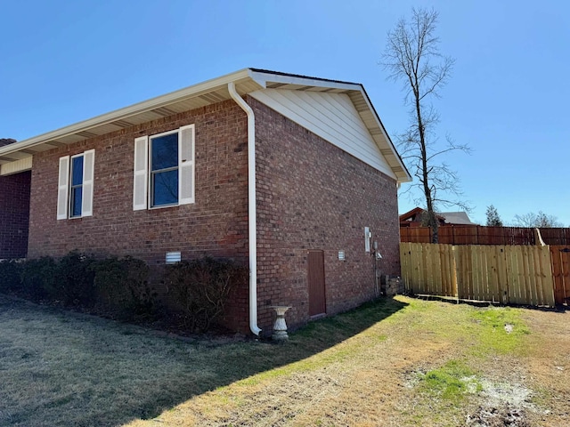 view of home's exterior featuring brick siding, a lawn, and fence