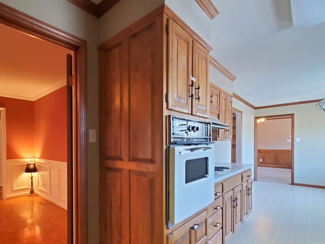 kitchen with white appliances, a wainscoted wall, ornamental molding, light countertops, and a decorative wall