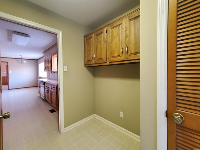 clothes washing area featuring baseboards, a chandelier, and crown molding