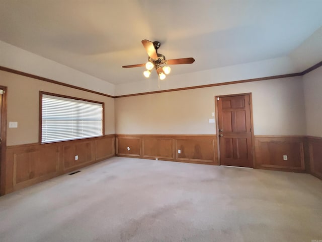 spare room featuring light colored carpet, a wainscoted wall, and ceiling fan