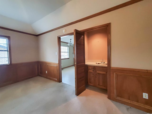 empty room with crown molding, a wainscoted wall, light colored carpet, vaulted ceiling, and a sink