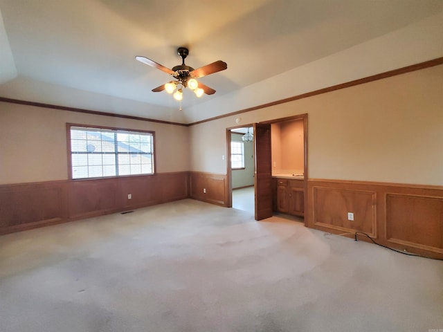 spare room with crown molding, a ceiling fan, a wainscoted wall, and light carpet