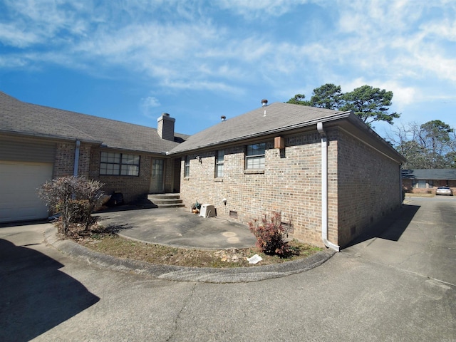 view of side of property featuring crawl space, brick siding, roof with shingles, and a chimney