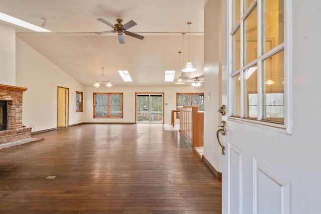 living area featuring a ceiling fan, dark wood-style floors, a skylight, baseboards, and a brick fireplace