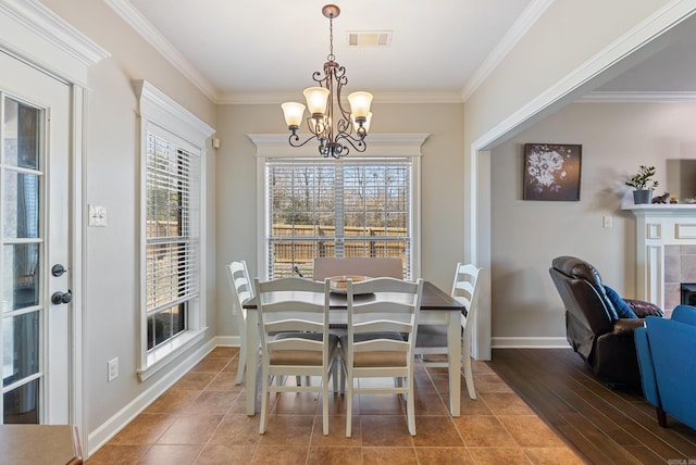 dining room featuring visible vents, crown molding, baseboards, a chandelier, and a tile fireplace