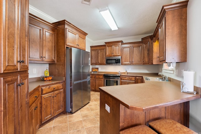 kitchen featuring brown cabinets, appliances with stainless steel finishes, a peninsula, a kitchen breakfast bar, and a sink