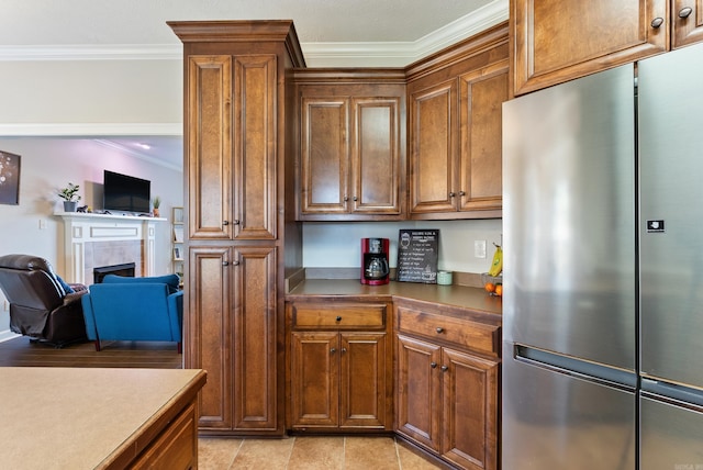 kitchen featuring brown cabinets, open floor plan, stainless steel fridge, a fireplace, and crown molding