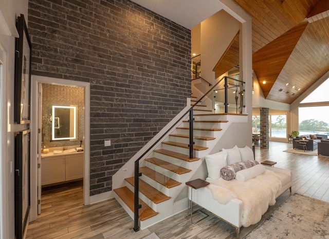 stairs featuring wooden ceiling, wood finished floors, brick wall, and vaulted ceiling