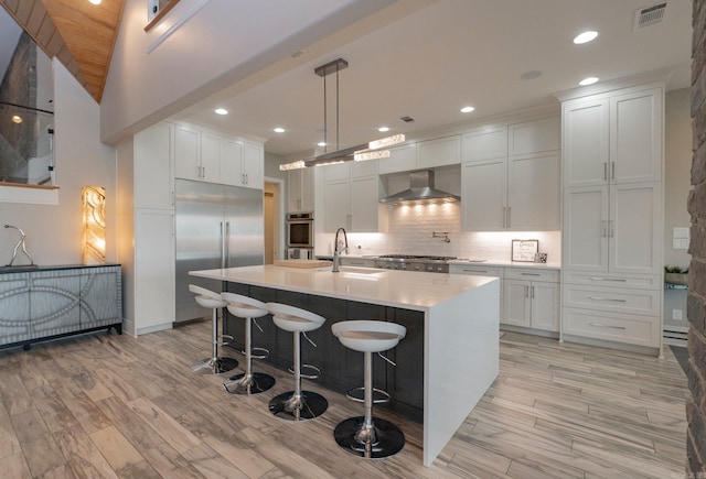 kitchen featuring a sink, wall chimney range hood, tasteful backsplash, stainless steel appliances, and light countertops