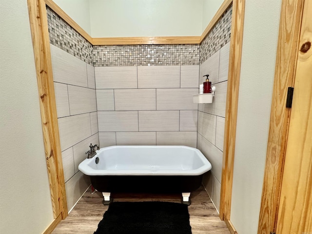 bathroom with a soaking tub, tile walls, and wood finished floors