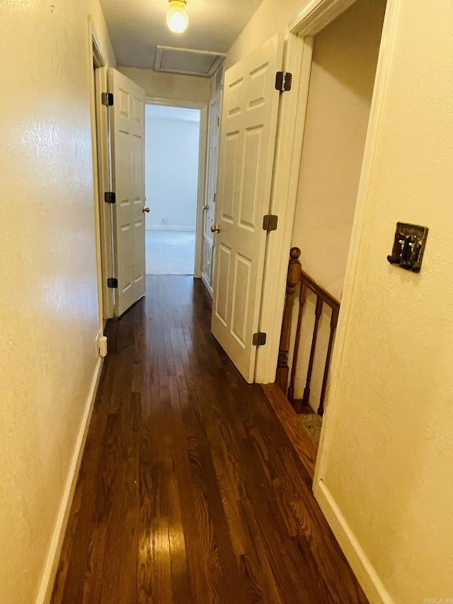 corridor featuring baseboards, attic access, and dark wood-style floors