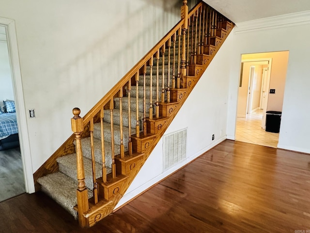 stairs featuring baseboards, wood finished floors, visible vents, and ornamental molding