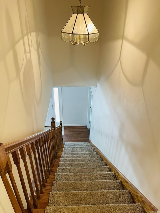 stairs featuring a notable chandelier, wood finished floors, and a towering ceiling