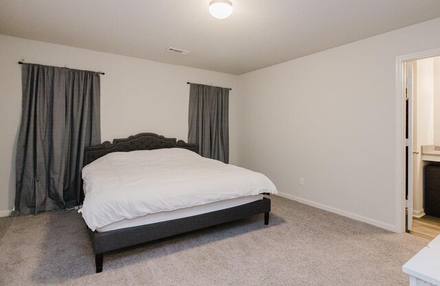 carpeted bedroom with visible vents, ensuite bathroom, and baseboards