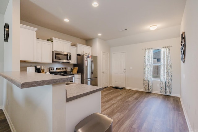 kitchen featuring baseboards, recessed lighting, appliances with stainless steel finishes, wood finished floors, and white cabinetry