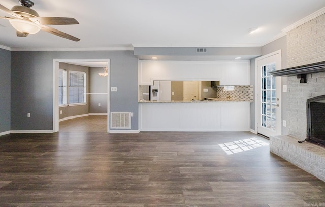 unfurnished living room with dark wood finished floors, visible vents, a brick fireplace, and crown molding