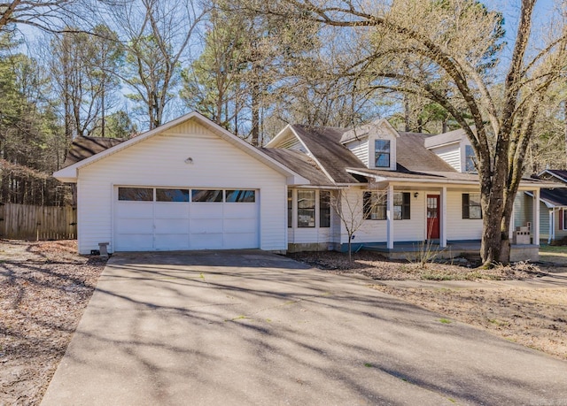 cape cod home featuring aphalt driveway, an attached garage, fence, and a porch