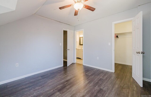 unfurnished bedroom featuring a walk in closet, vaulted ceiling, dark wood-style floors, and baseboards