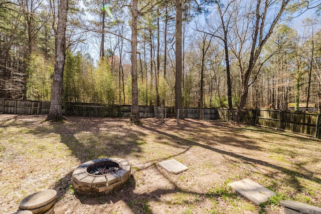 view of yard with a view of trees, a fire pit, and a fenced backyard