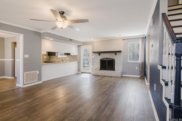 unfurnished living room with visible vents, dark wood finished floors, a fireplace, stairs, and crown molding