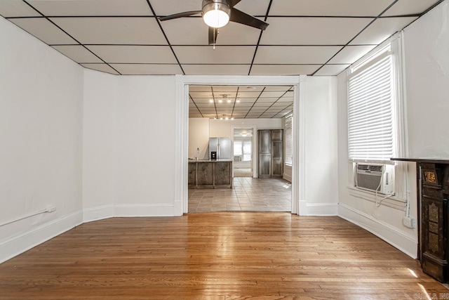 interior space featuring light wood-type flooring, a ceiling fan, a drop ceiling, cooling unit, and baseboards