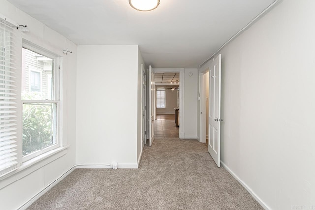 corridor featuring light colored carpet and baseboards