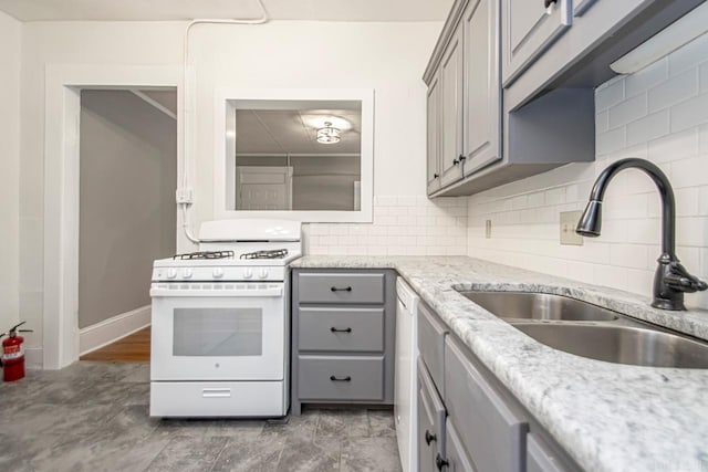 kitchen featuring gray cabinetry, white gas range, decorative backsplash, light stone counters, and a sink