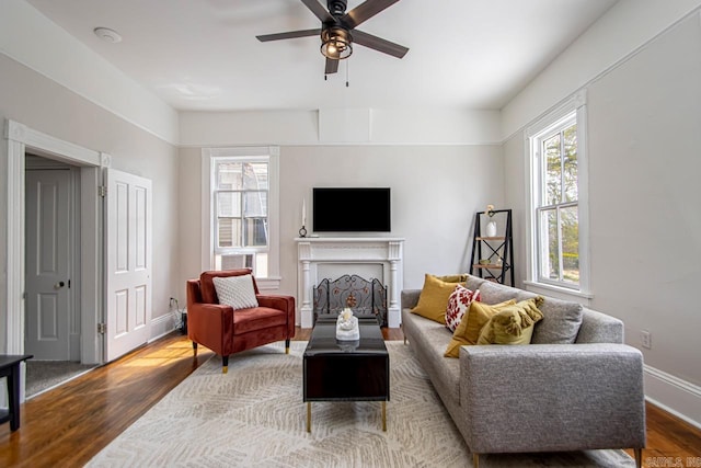 living room featuring ceiling fan, baseboards, wood finished floors, and a fireplace