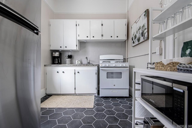 kitchen with dark tile patterned flooring, gas range gas stove, tasteful backsplash, white cabinets, and black microwave