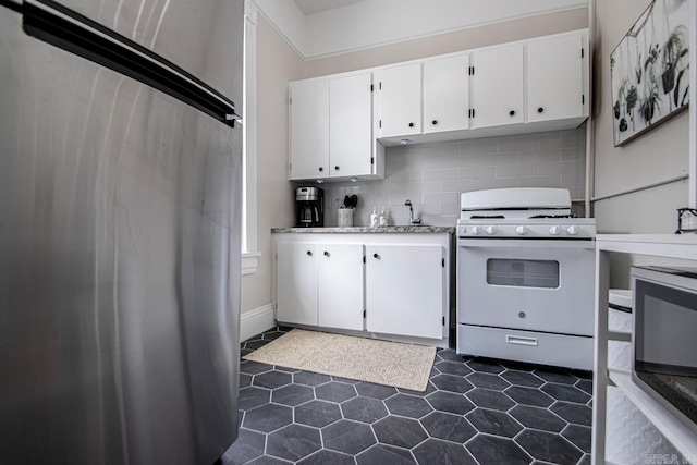 kitchen featuring light countertops, white range with gas cooktop, decorative backsplash, white cabinets, and fridge