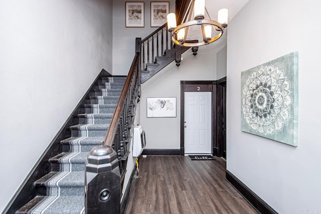 foyer entrance featuring dark wood-style floors, baseboards, a high ceiling, stairs, and a chandelier