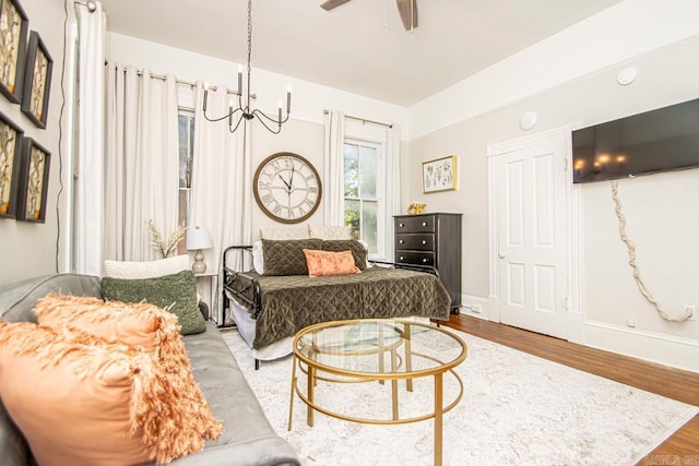 bedroom featuring ceiling fan with notable chandelier, wood finished floors, and baseboards