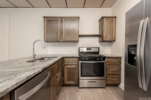 kitchen featuring a sink, stainless steel appliances, light stone counters, and tasteful backsplash