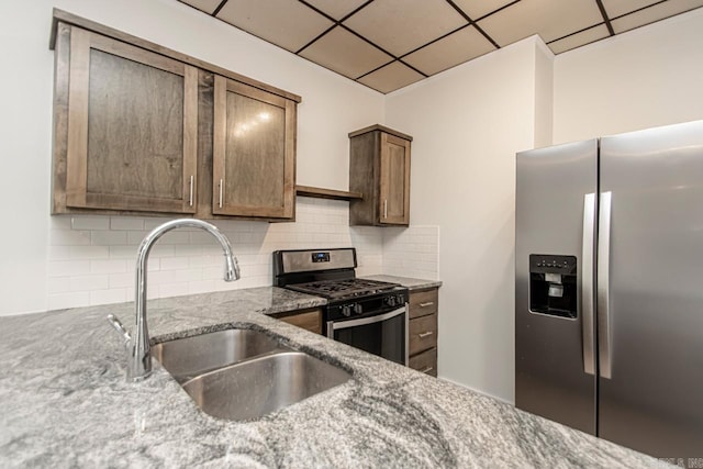 kitchen with light stone countertops, a drop ceiling, a sink, decorative backsplash, and appliances with stainless steel finishes