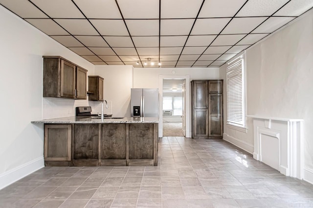 kitchen featuring a sink, dark brown cabinetry, a peninsula, stainless steel fridge with ice dispenser, and light stone countertops