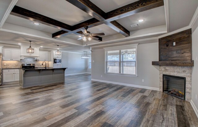 unfurnished living room featuring beamed ceiling, a sink, dark wood finished floors, a stone fireplace, and baseboards