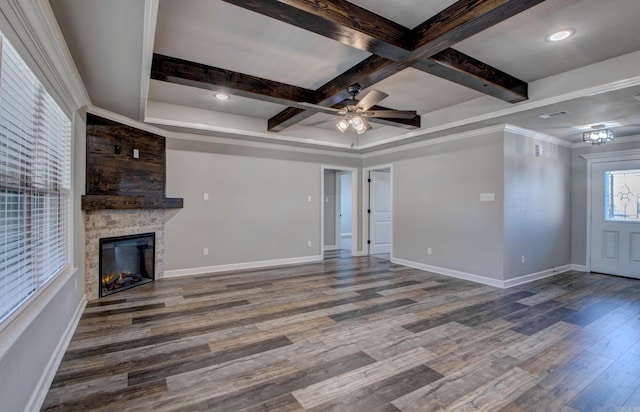 unfurnished living room featuring a stone fireplace, beam ceiling, wood finished floors, and baseboards