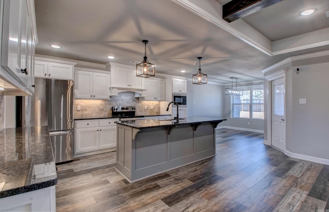 kitchen with wood finished floors, under cabinet range hood, appliances with stainless steel finishes, crown molding, and backsplash