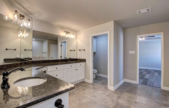 bathroom with baseboards, visible vents, double vanity, a sink, and toilet