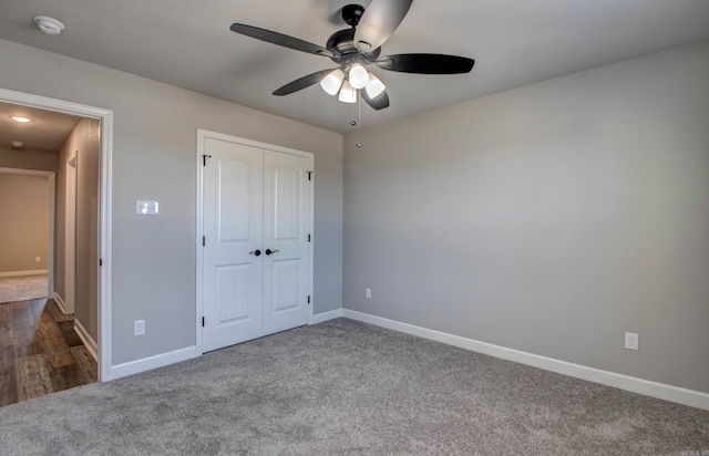 unfurnished bedroom with dark colored carpet, a closet, baseboards, and ceiling fan