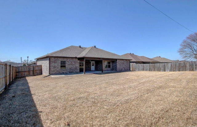 rear view of property with a patio, a yard, a fenced backyard, a shingled roof, and brick siding