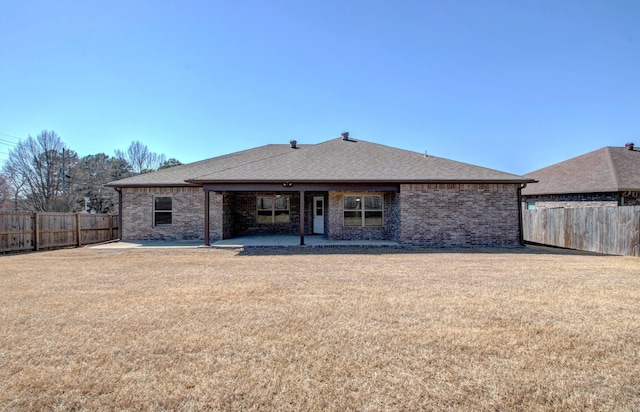 rear view of property featuring a yard, a fenced backyard, brick siding, and a patio