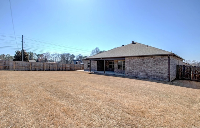 rear view of property with brick siding, a fenced backyard, a lawn, and a shingled roof