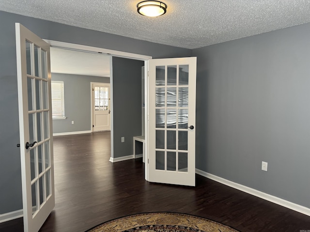 empty room featuring wood finished floors, baseboards, french doors, and a textured ceiling