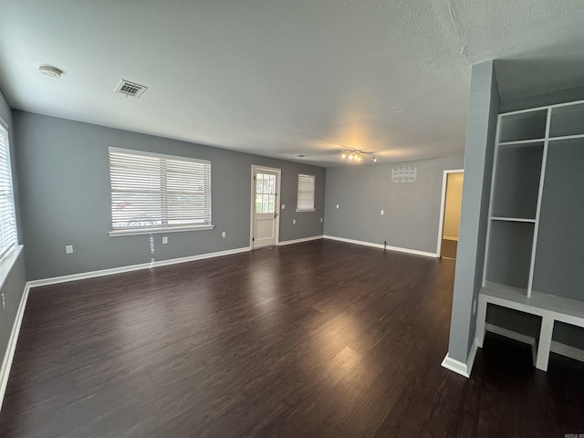 unfurnished living room featuring visible vents, a textured ceiling, baseboards, and wood finished floors