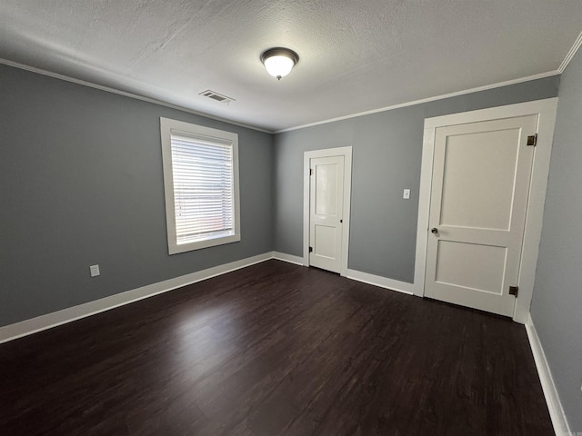 unfurnished bedroom featuring visible vents, baseboards, dark wood-style floors, and crown molding