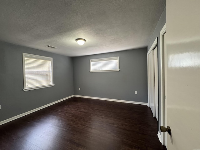 unfurnished bedroom featuring visible vents, a textured ceiling, baseboards, and dark wood-style flooring